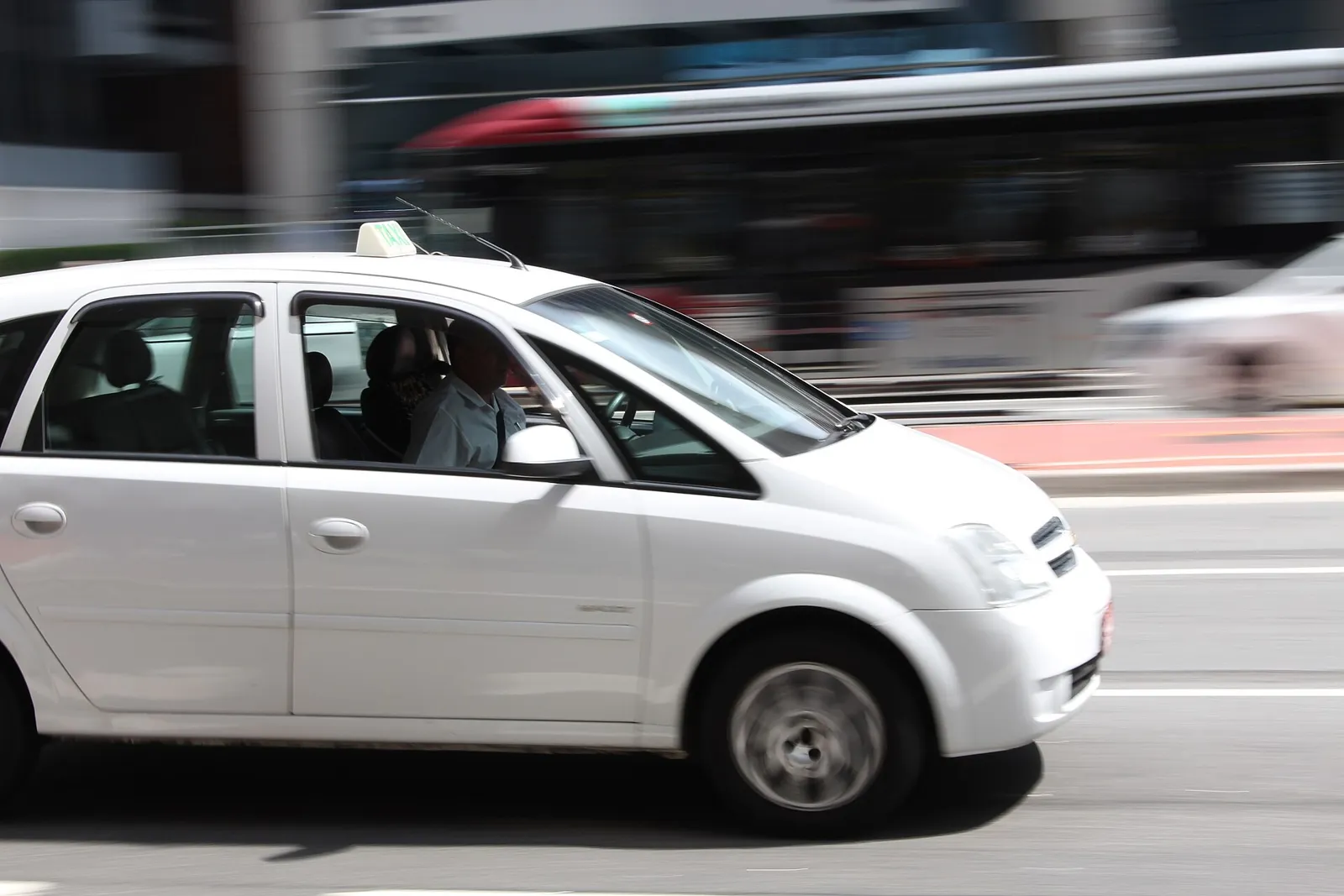 Táxi branco circulando por avenida movimentada